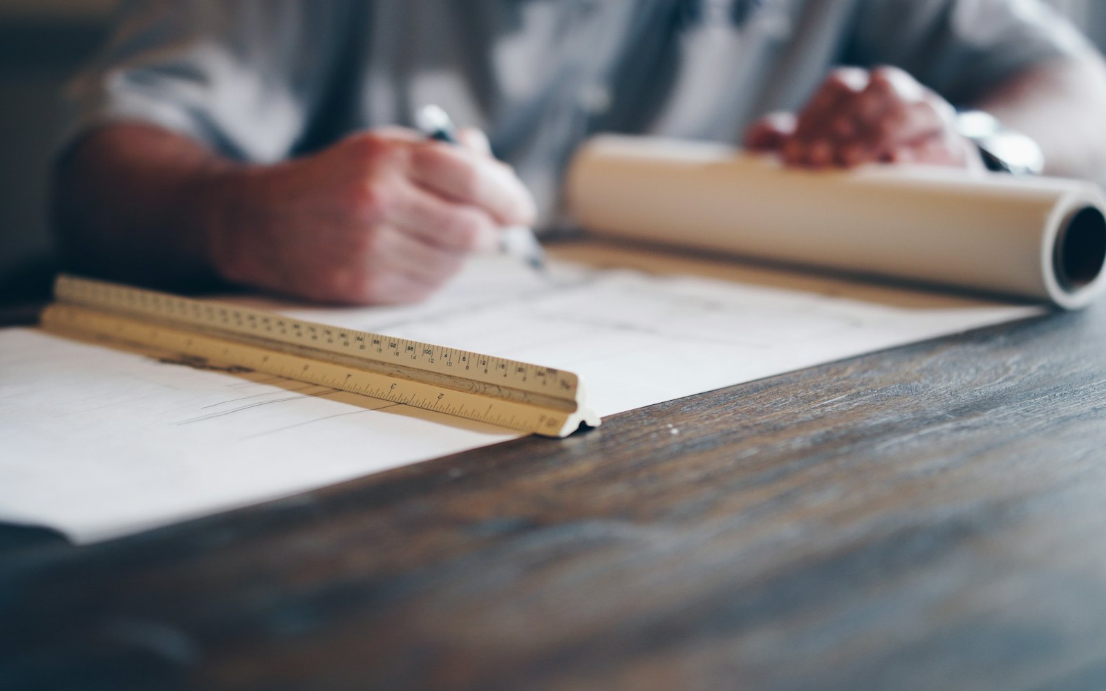 Marking up a set of plans at a desk with a scale rule, a rolled drawing to one side